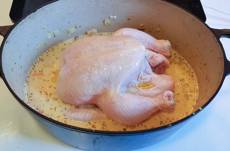 A chicken added to a sauce pot and ready to roast