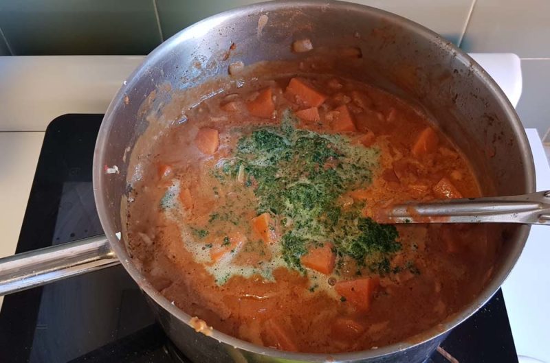 adding spinach to sweet potatoes in a pot