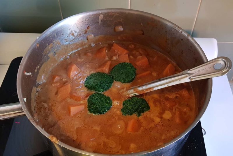 adding frozen spinach to a pot of stew
