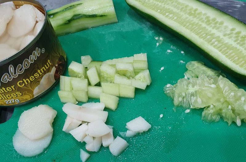 A chopping board with cucumber and water chestnuts